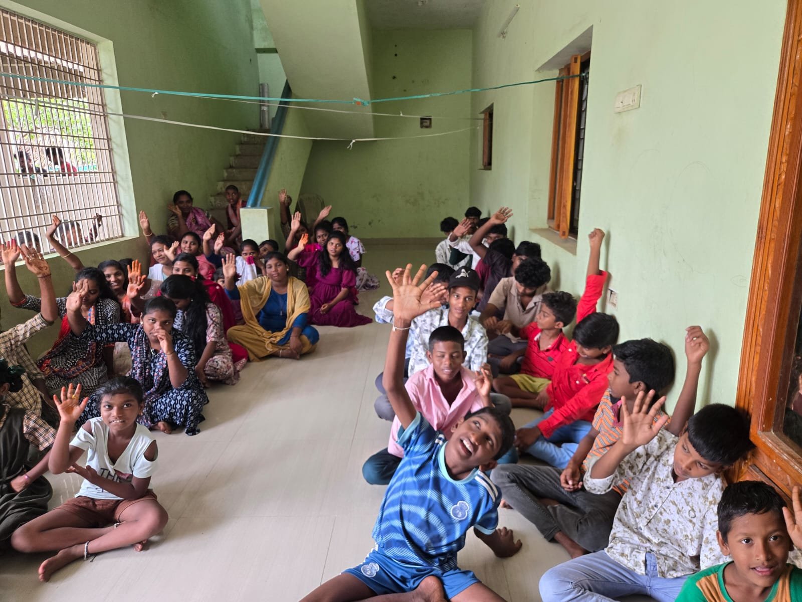 Children and young people seated on the floor of a hall with their hands raised, smiling